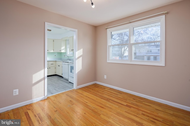 spare room featuring a sink, light wood-type flooring, and baseboards