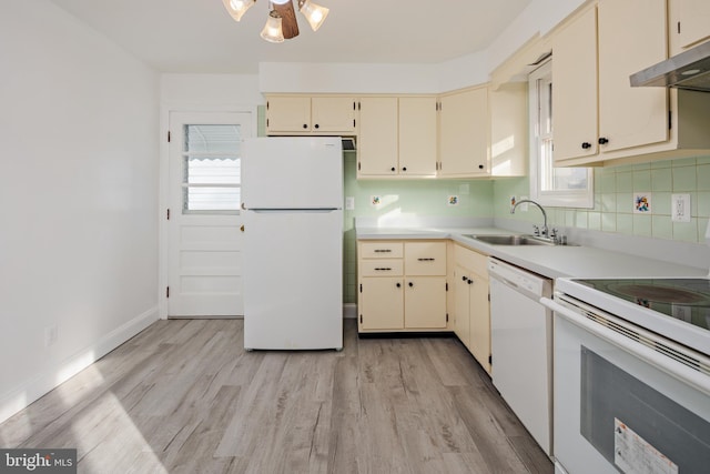 kitchen with under cabinet range hood, white appliances, cream cabinetry, and a sink