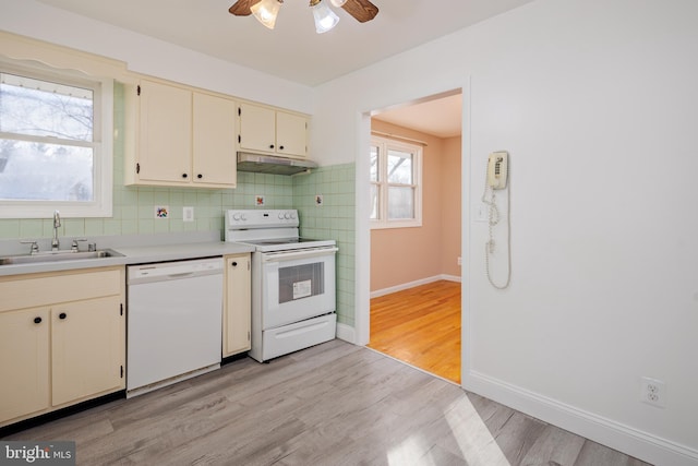 kitchen with white appliances, light wood-style flooring, a sink, under cabinet range hood, and tasteful backsplash