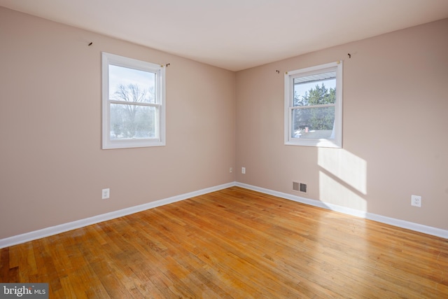 empty room featuring visible vents, light wood-type flooring, and baseboards