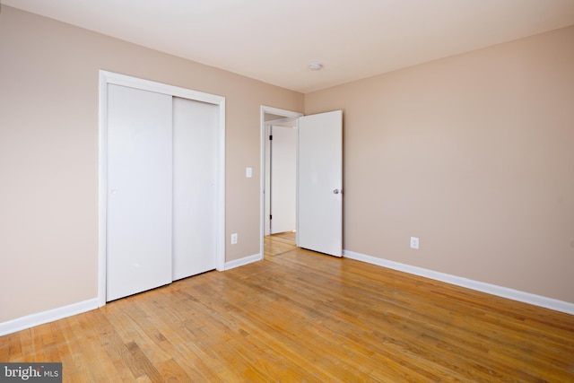 unfurnished bedroom featuring light wood-style flooring, baseboards, and a closet