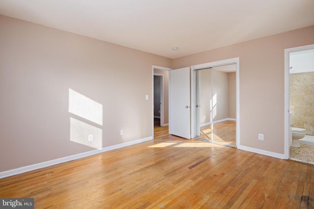 unfurnished bedroom with a closet, baseboards, light wood-style floors, and ensuite bathroom