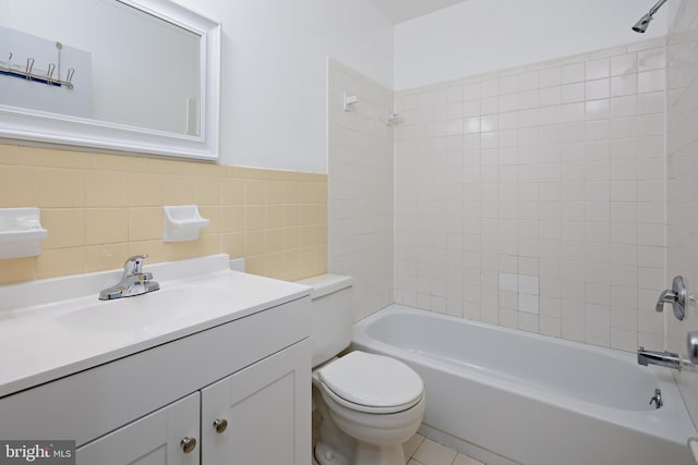 bathroom featuring a wainscoted wall, toilet, tile walls, bathtub / shower combination, and vanity