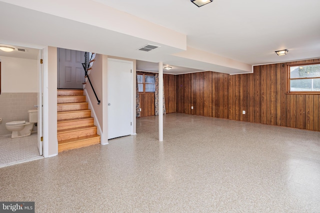 basement with visible vents, wooden walls, wainscoting, and stairs