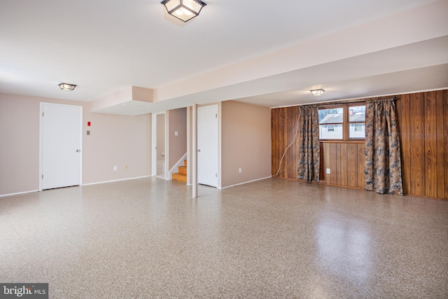 empty room featuring wooden walls, stairs, speckled floor, and baseboards