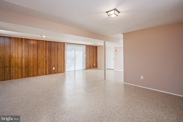 spare room featuring speckled floor, baseboards, and wood walls