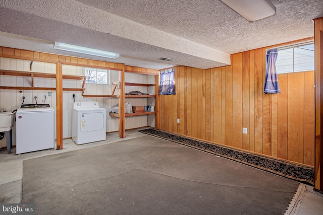 basement with a textured ceiling, wooden walls, visible vents, and washing machine and clothes dryer