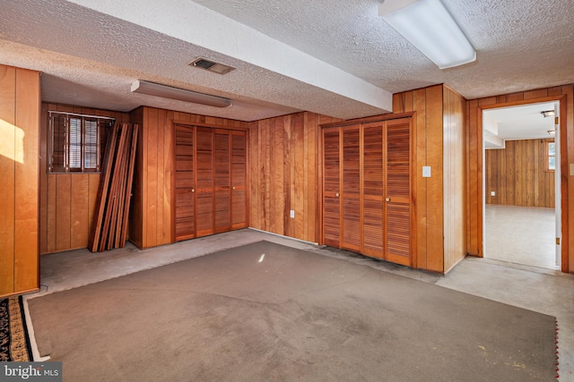 finished basement with visible vents, a textured ceiling, and wood walls