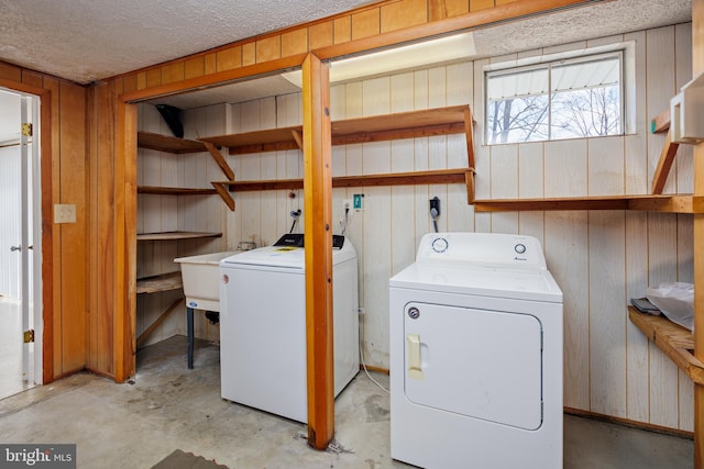 laundry room featuring laundry area, separate washer and dryer, a sink, wood walls, and a textured ceiling