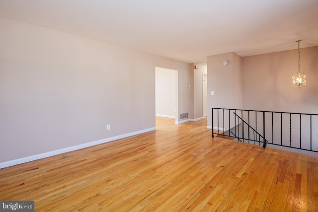 empty room featuring a chandelier, visible vents, baseboards, and light wood-style floors