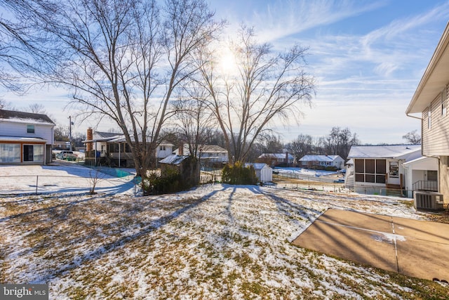 yard layered in snow with a residential view, a shed, central AC, an outdoor structure, and a sunroom