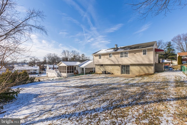 snow covered back of property featuring central AC unit, fence, and a sunroom