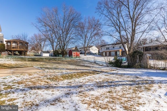 yard covered in snow featuring a residential view, a storage unit, an outdoor structure, and fence