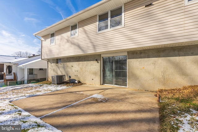 snow covered rear of property with central air condition unit and a patio area