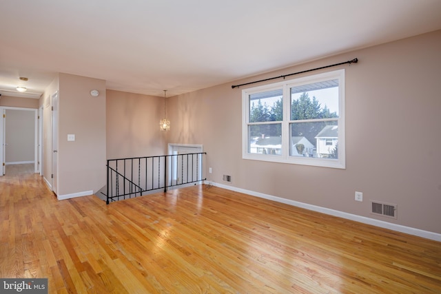 empty room with visible vents, baseboards, a notable chandelier, and light wood finished floors