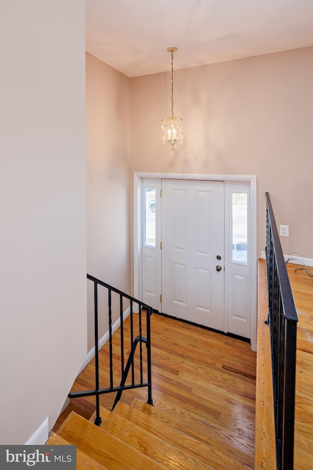 foyer featuring baseboards, a notable chandelier, stairs, and light wood finished floors