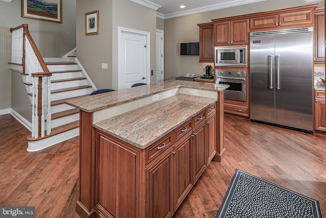 kitchen featuring light stone counters, a center island, ornamental molding, wood finished floors, and built in appliances