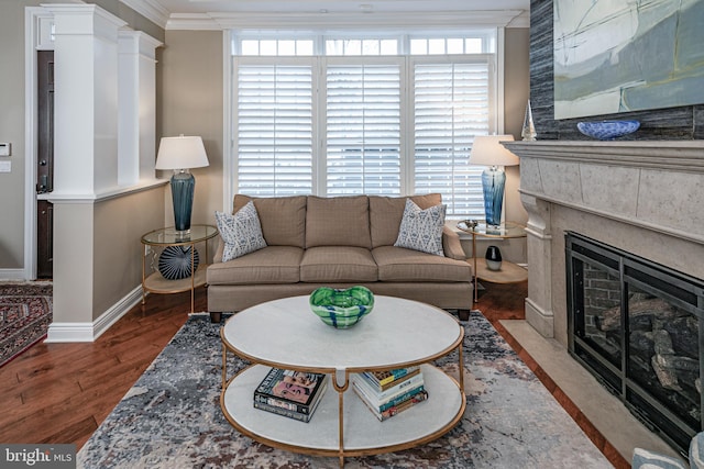 living room with a large fireplace, crown molding, baseboards, and wood finished floors