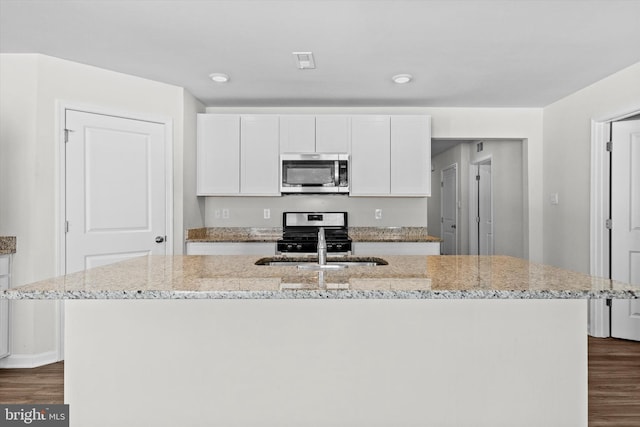 kitchen featuring white cabinetry, light stone counters, a center island with sink, and appliances with stainless steel finishes