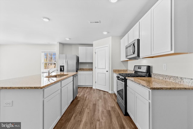 kitchen with sink, appliances with stainless steel finishes, white cabinetry, an island with sink, and light wood-type flooring