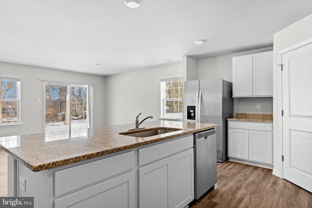 kitchen featuring sink, appliances with stainless steel finishes, a kitchen island with sink, white cabinetry, and light stone counters