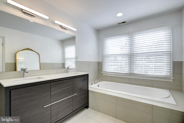 bathroom featuring a relaxing tiled tub, vanity, and tile patterned flooring