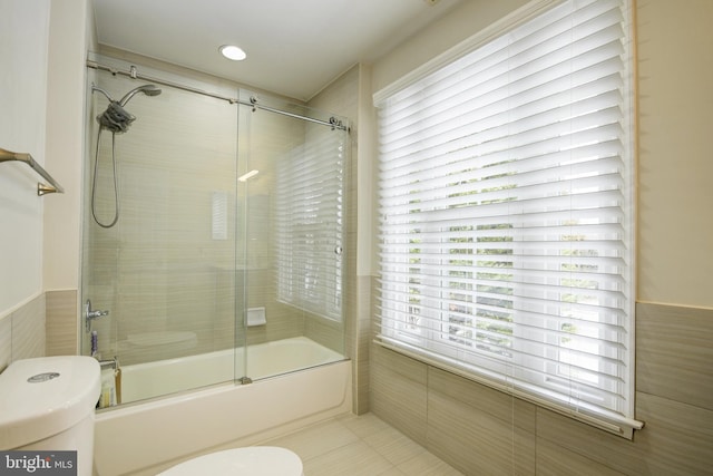 bathroom featuring tile patterned flooring, combined bath / shower with glass door, tile walls, and toilet