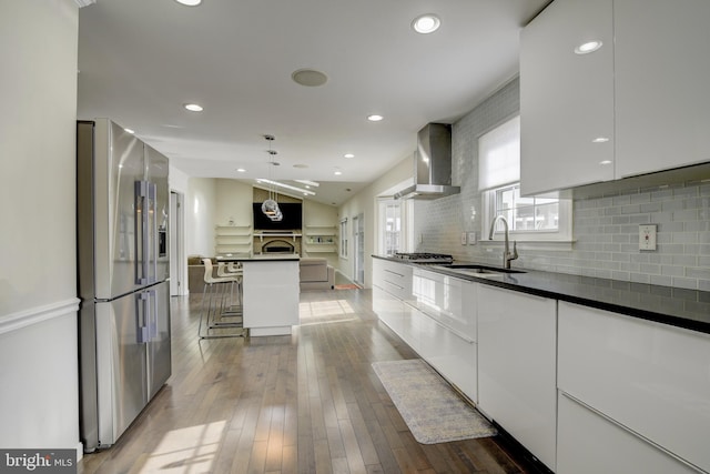 kitchen with stainless steel appliances, a kitchen breakfast bar, white cabinets, a kitchen island, and wall chimney exhaust hood