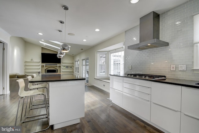 kitchen featuring white cabinetry, a kitchen island, decorative light fixtures, vaulted ceiling, and wall chimney exhaust hood