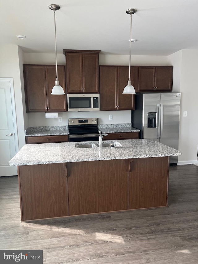 kitchen with light stone countertops, stainless steel appliances, and a center island with sink