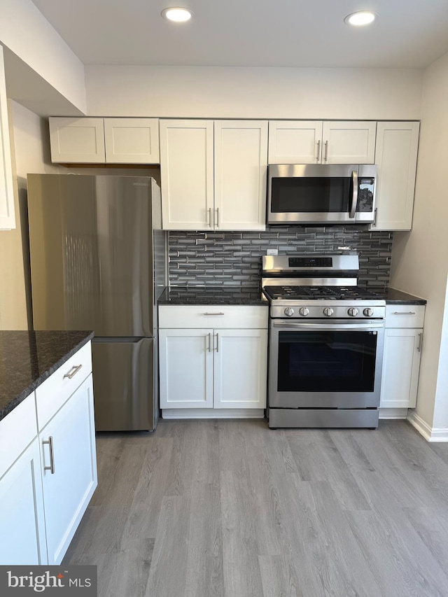 kitchen with tasteful backsplash, white cabinetry, dark stone countertops, stainless steel appliances, and light hardwood / wood-style flooring