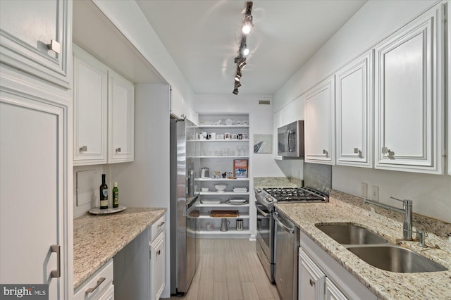 kitchen with stainless steel appliances, light stone countertops, sink, and white cabinets