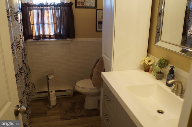 bathroom with tile walls, hardwood / wood-style flooring, vanity, a baseboard heating unit, and toilet