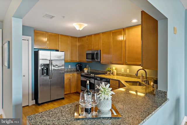 kitchen with stainless steel appliances, stone counters, a peninsula, and a sink