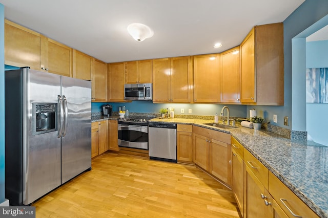 kitchen featuring stainless steel appliances, light wood-style floors, a sink, and dark stone countertops