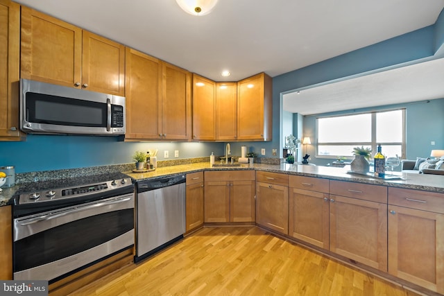 kitchen with light wood finished floors, appliances with stainless steel finishes, dark stone countertops, and a sink