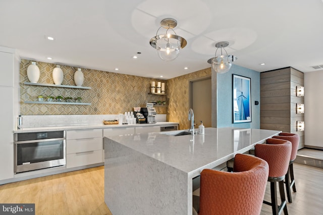 kitchen featuring light wood finished floors, modern cabinets, oven, white cabinetry, and a sink