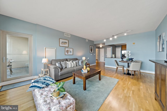 living room featuring light wood finished floors, track lighting, visible vents, and baseboards