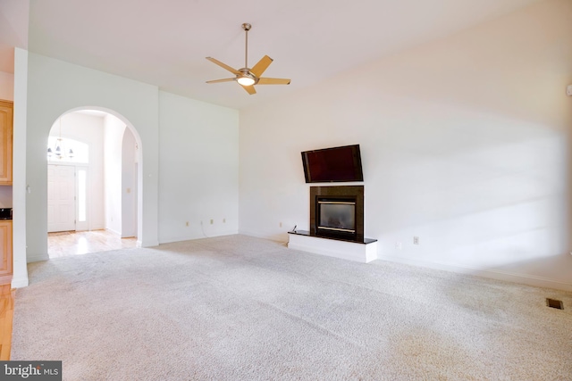 unfurnished living room featuring ceiling fan, light colored carpet, arched walkways, baseboards, and a glass covered fireplace