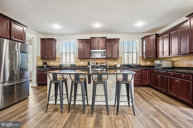 kitchen featuring dark wood-type flooring, a breakfast bar area, backsplash, and appliances with stainless steel finishes