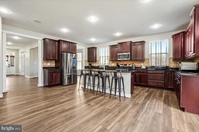kitchen with stainless steel appliances, a kitchen breakfast bar, dark countertops, and a healthy amount of sunlight