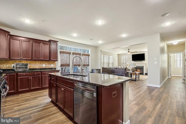 kitchen featuring wood finished floors, a warm lit fireplace, a sink, decorative backsplash, and stainless steel appliances