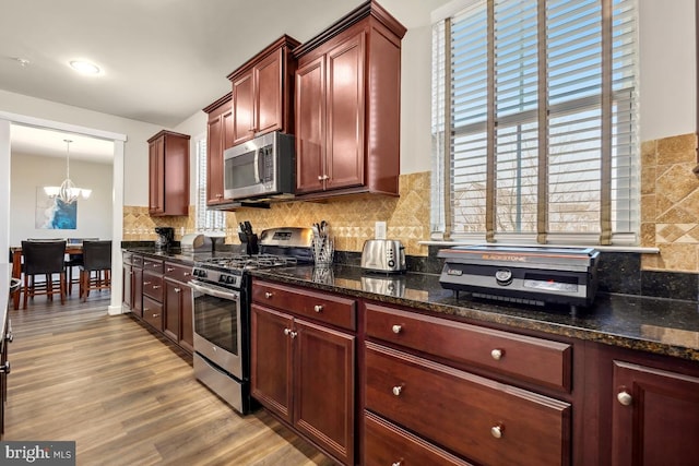 kitchen with wood finished floors, stainless steel appliances, decorative backsplash, dark brown cabinets, and a notable chandelier