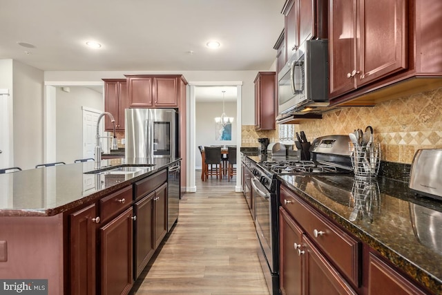 kitchen featuring tasteful backsplash, light wood-style flooring, appliances with stainless steel finishes, a notable chandelier, and a sink
