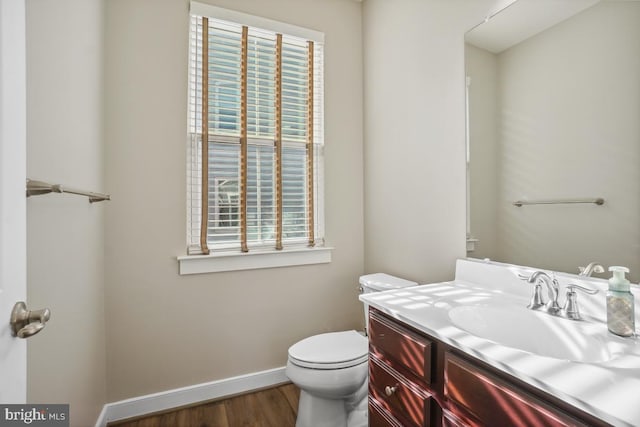 half bath featuring baseboards, toilet, wood finished floors, and vanity