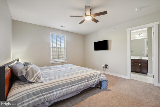 bedroom featuring visible vents, light carpet, ensuite bathroom, a sink, and baseboards