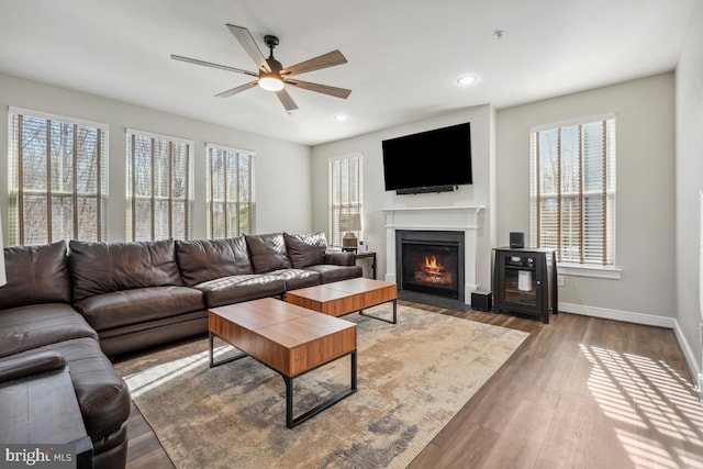 living room with baseboards, a fireplace with flush hearth, recessed lighting, wood finished floors, and a ceiling fan