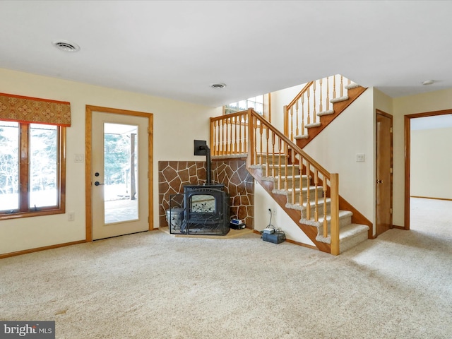 unfurnished living room featuring visible vents, stairway, carpet, and a wood stove