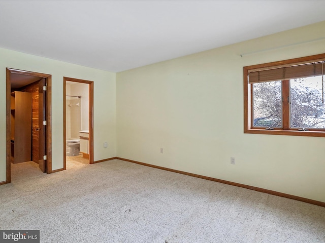 unfurnished bedroom with light carpet, ensuite bathroom, and baseboards