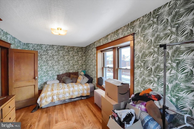 bedroom featuring radiator, light hardwood / wood-style flooring, and a textured ceiling